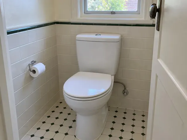 Clean white toilet in a tiled bathroom with a window and patterned floor in Artarmon
